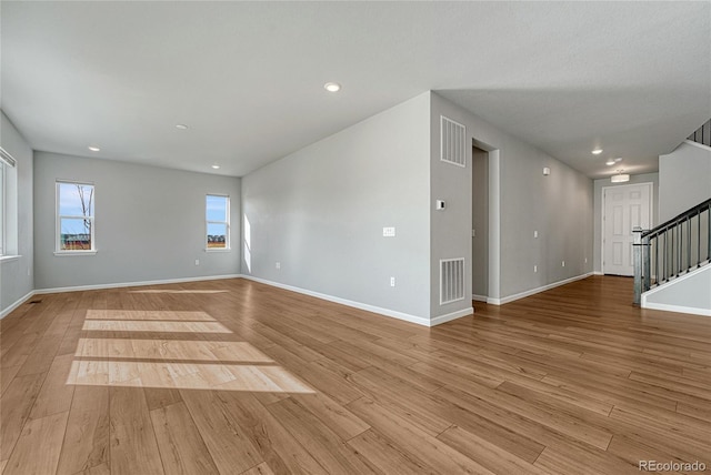 empty room with light wood-type flooring, visible vents, baseboards, and stairs