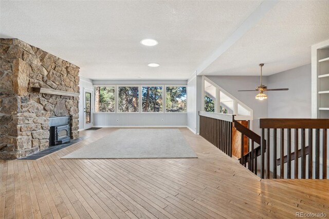 4835 Abo Ln, Monument, CO 80132 - unfurnished living room with ceiling fan, a wood stove, a textured ceiling, hardwood / wood-style floors, and baseboards