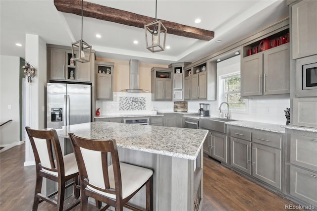 kitchen featuring pendant lighting, sink, stainless steel appliances, a kitchen island, and wall chimney exhaust hood