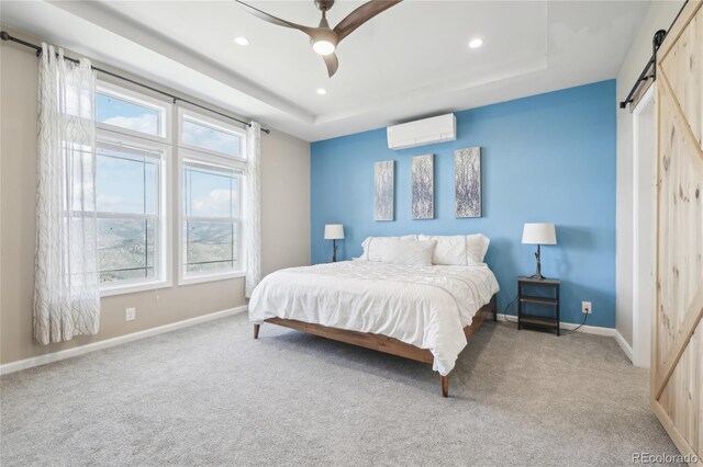 carpeted bedroom with ceiling fan, a barn door, a wall unit AC, and a tray ceiling