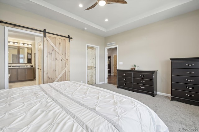 bedroom with ceiling fan, a barn door, light colored carpet, and ensuite bath