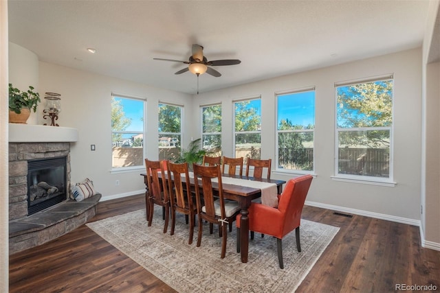 dining space with ceiling fan, a fireplace, a healthy amount of sunlight, and dark hardwood / wood-style flooring