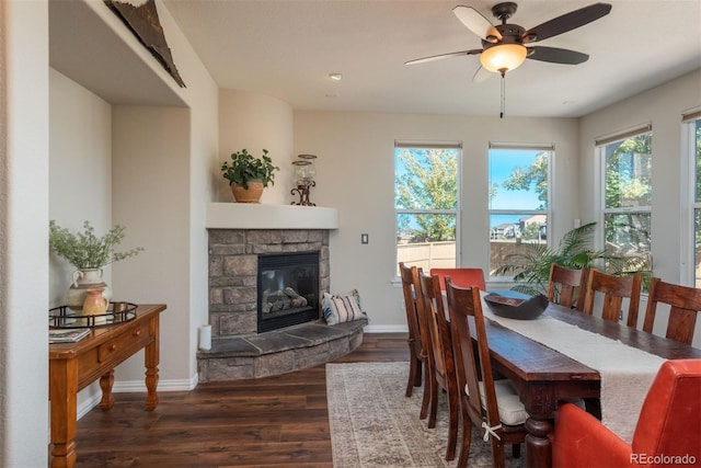 dining area with ceiling fan, a stone fireplace, dark hardwood / wood-style floors, and a healthy amount of sunlight