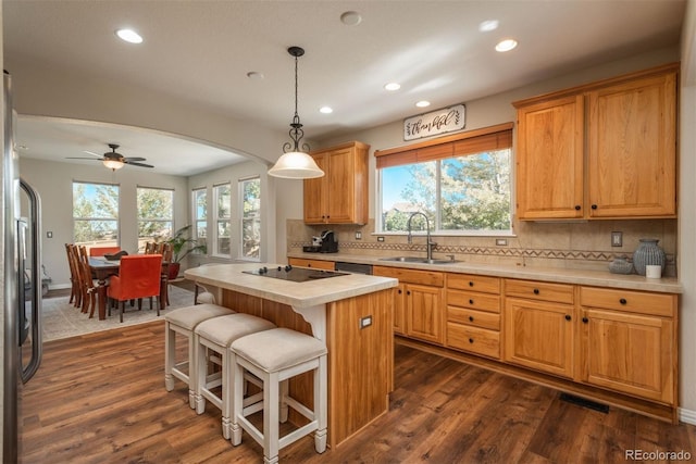 kitchen featuring hanging light fixtures, a kitchen island, dark hardwood / wood-style flooring, ceiling fan, and sink