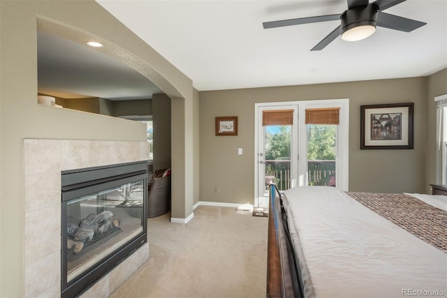 carpeted bedroom with ceiling fan, access to outside, and a tile fireplace