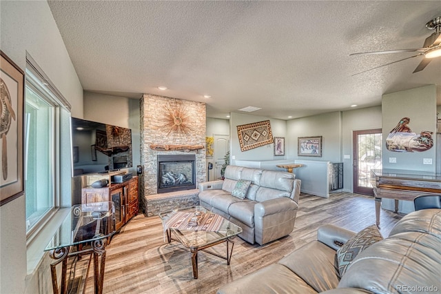 living room with a stone fireplace, ceiling fan, a textured ceiling, and hardwood / wood-style flooring