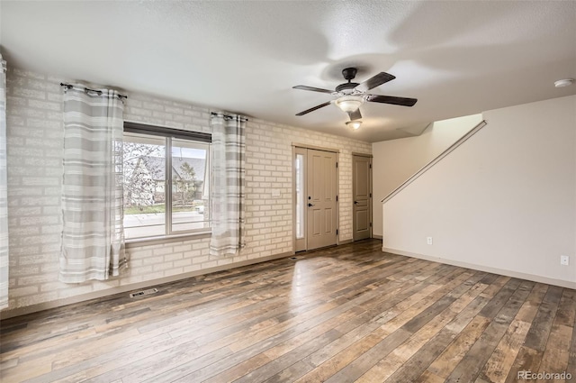 empty room featuring brick wall, hardwood / wood-style flooring, and ceiling fan