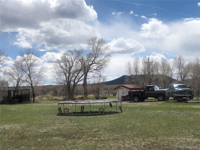view of grassy yard featuring a trampoline and a mountain view