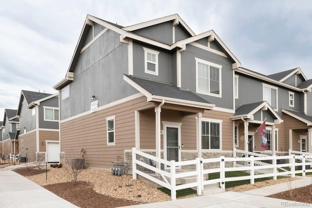 view of front of property with central AC unit, a fenced front yard, and stone siding
