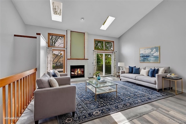 living area featuring a fireplace, a skylight, high vaulted ceiling, and wood finished floors