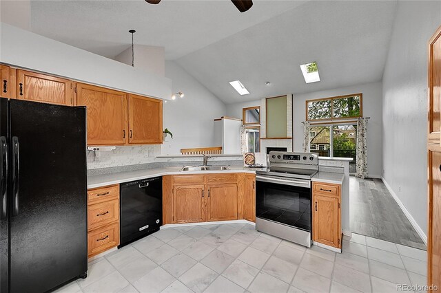 kitchen with a sink, a peninsula, vaulted ceiling with skylight, black appliances, and light countertops