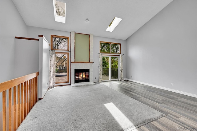 unfurnished living room with a fireplace, lofted ceiling with skylight, baseboards, and wood finished floors