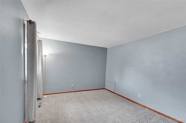 carpeted spare room with a textured ceiling, visible vents, and baseboards
