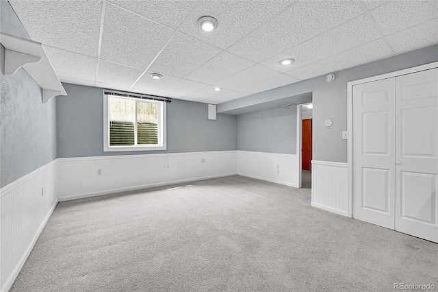 basement featuring a drop ceiling, carpet flooring, and a wainscoted wall