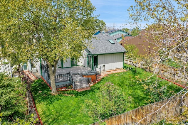 rear view of house featuring a shingled roof, a wooden deck, a lawn, and a fenced backyard