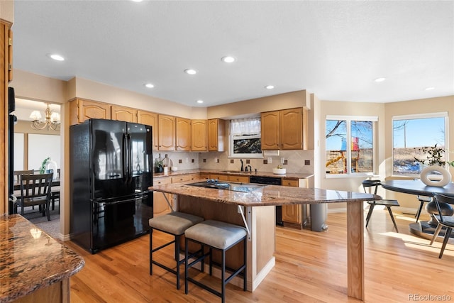 kitchen featuring light stone countertops, black appliances, a kitchen island, decorative backsplash, and a breakfast bar