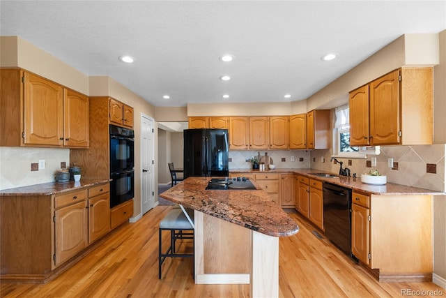 kitchen featuring a center island, black appliances, sink, light wood-type flooring, and a kitchen breakfast bar