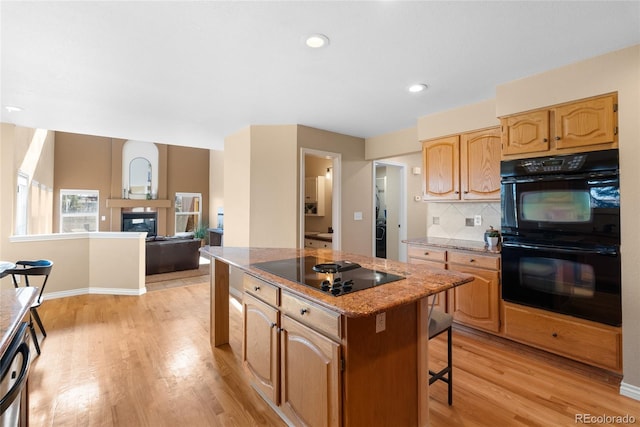 kitchen featuring black appliances, a center island, a kitchen bar, light hardwood / wood-style floors, and decorative backsplash