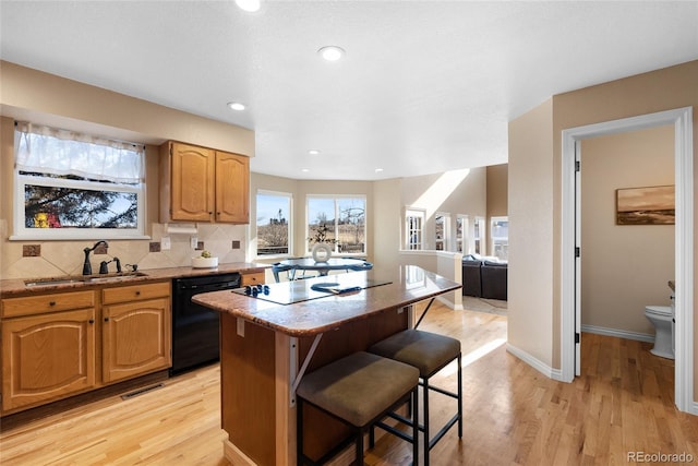 kitchen with black appliances, a kitchen bar, light hardwood / wood-style floors, sink, and backsplash