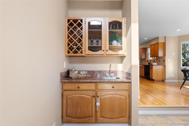 bar with sink, black dishwasher, dark stone counters, and light tile patterned flooring