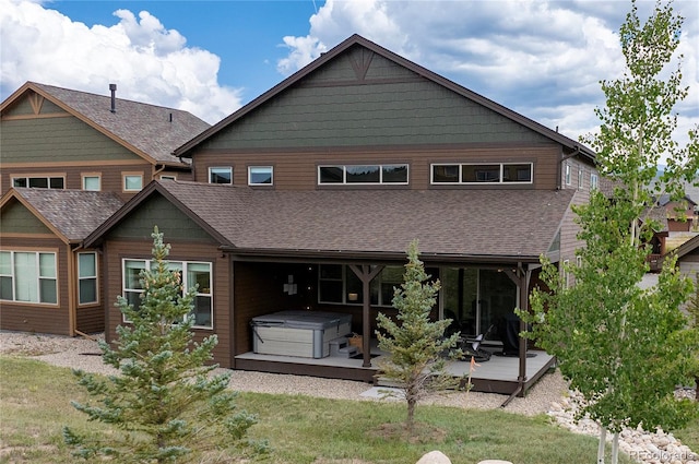 rear view of house with a hot tub, a wooden deck, and a yard