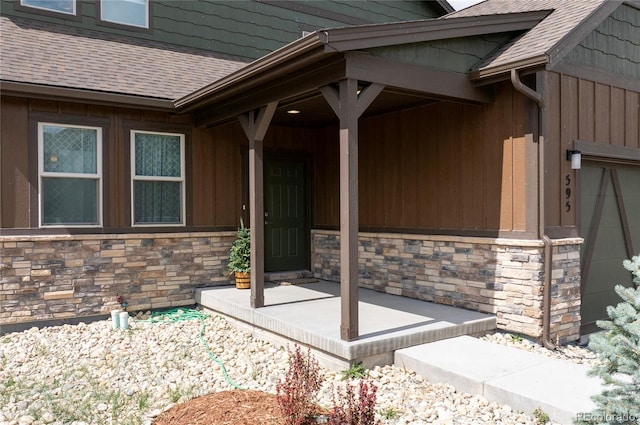 entrance to property featuring a porch, a shingled roof, and stone siding