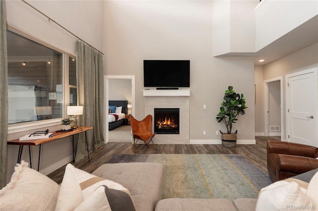 living room featuring baseboards, a towering ceiling, wood finished floors, and a fireplace