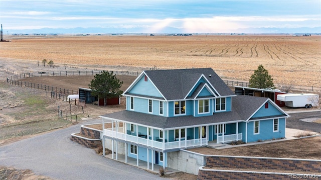 view of front facade featuring a shingled roof, covered porch, a rural view, and driveway