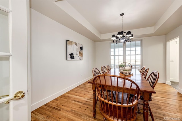 dining room with a chandelier, a tray ceiling, light wood-style floors, and baseboards