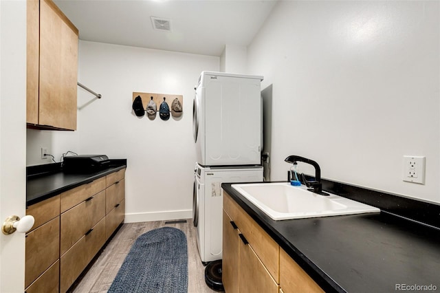 laundry room with a sink, visible vents, light wood-type flooring, stacked washing maching and dryer, and cabinet space