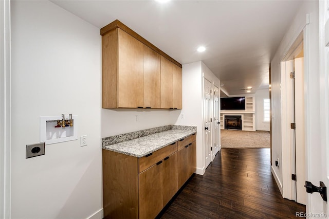 kitchen with a fireplace, baseboards, open floor plan, light stone countertops, and dark wood finished floors