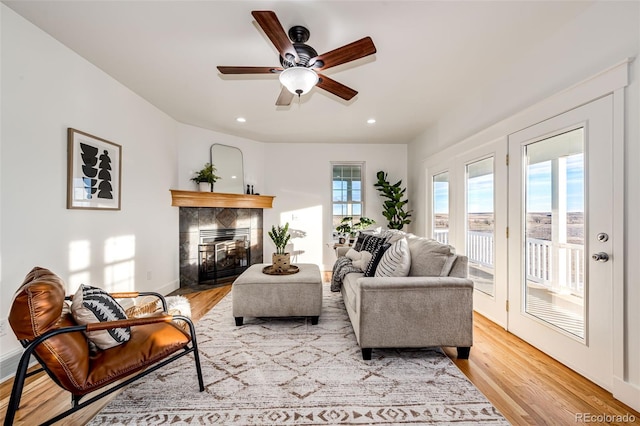 living area with light wood-style floors, a tile fireplace, a ceiling fan, and recessed lighting