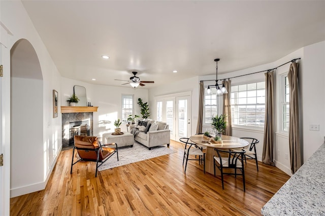 living room featuring arched walkways, a fireplace, recessed lighting, light wood-style flooring, and baseboards