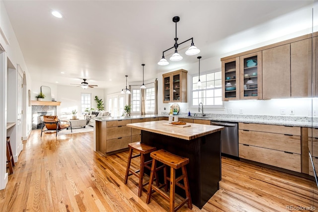 kitchen featuring a peninsula, stainless steel dishwasher, light wood-style floors, a fireplace, and a sink