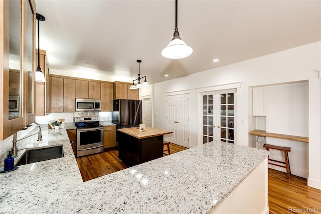 kitchen featuring dark wood-style floors, appliances with stainless steel finishes, decorative light fixtures, french doors, and a sink