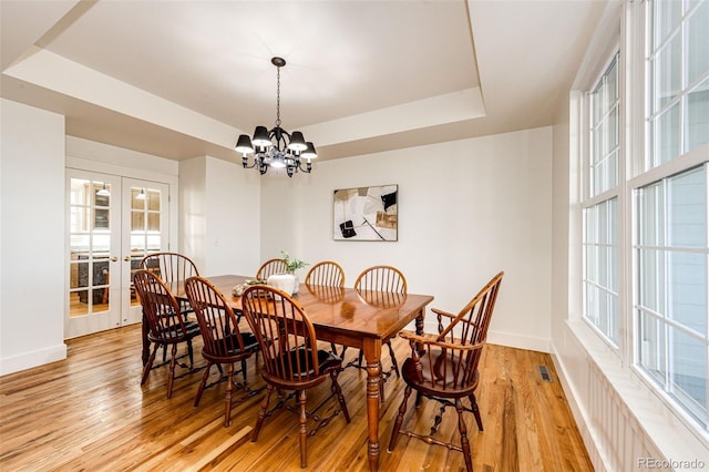 dining room featuring light wood-style floors, baseboards, a tray ceiling, and french doors