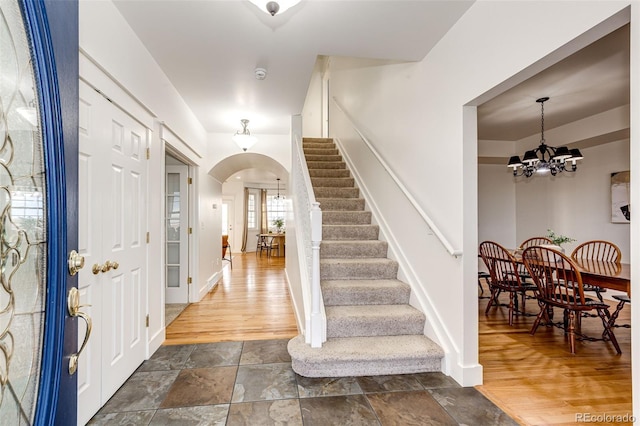 entrance foyer with baseboards, arched walkways, stone finish flooring, stairs, and a notable chandelier