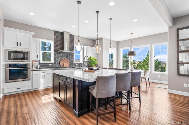 9563 Red Primrose St, Franktown, CO 80116 - kitchen with appliances with stainless steel finishes, wall chimney range hood, tasteful backsplash, a center island, and light wood-style flooring