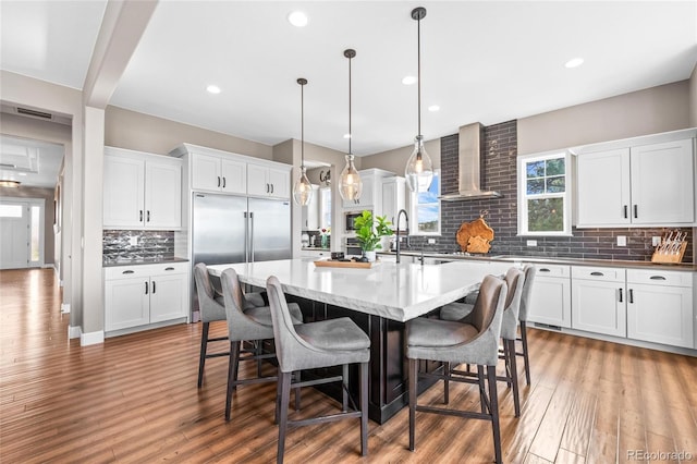 9563 Red Primrose St, Franktown, CO 80116 - kitchen featuring wall chimney range hood, built in fridge, decorative backsplash, an island with sink, and light wood-style floors