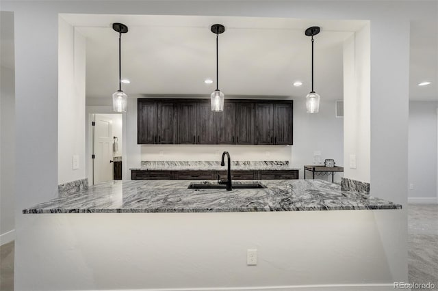 16510 Early Light Dr, Colorado Springs, CO 80908 - kitchen with dark brown cabinetry, hanging light fixtures, a sink, stone countertops, and a peninsula
