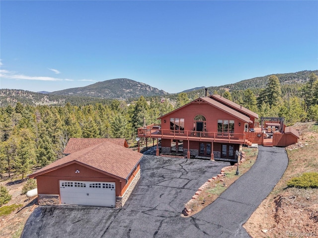 10786 Marclif Rd, Conifer, CO 80433 - view of front facade with a forest view, stone siding, a deck with mountain view, a garage, and driveway