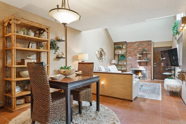 dining room with tile patterned floors, vaulted ceiling, a brick fireplace, and a textured ceiling