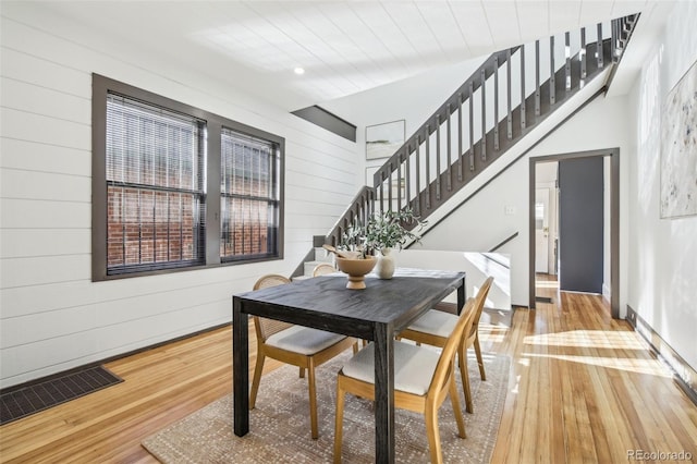 dining space with stairway, visible vents, wood-type flooring, and wooden walls