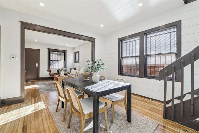 dining space with baseboards, wooden walls, light wood finished floors, recessed lighting, and stairs
