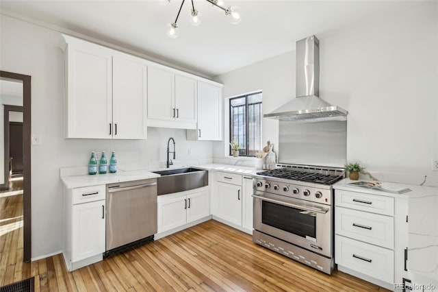 kitchen featuring visible vents, a sink, wall chimney range hood, light wood finished floors, and stainless steel appliances