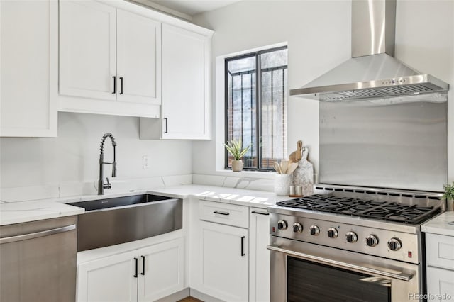 kitchen featuring wall chimney exhaust hood, high end stove, white cabinetry, light stone counters, and a sink