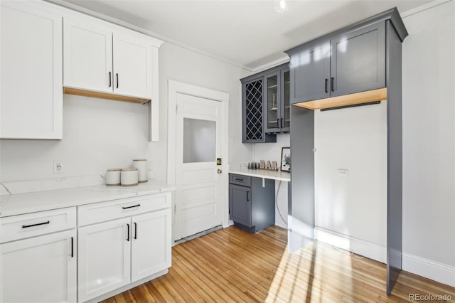 kitchen with glass insert cabinets, light wood-style flooring, white cabinetry, light countertops, and baseboards