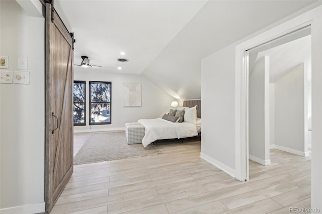 bedroom with a barn door, visible vents, light wood-type flooring, and lofted ceiling