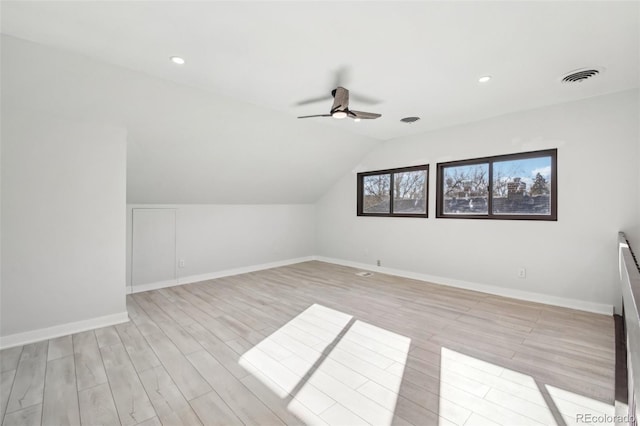 additional living space featuring baseboards, light wood-type flooring, vaulted ceiling, visible vents, and ceiling fan