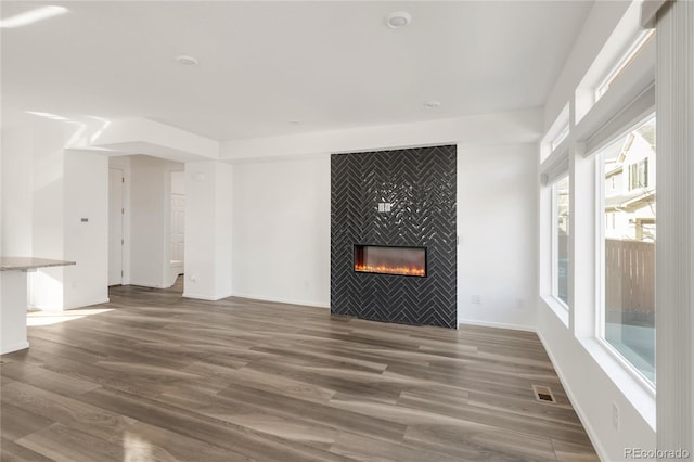 unfurnished living room with visible vents, a fireplace, baseboards, and wood finished floors